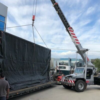 Mobile crane loading a tarp-wrapped load onto a flatbed truck